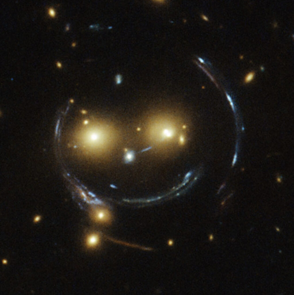 In the center of this image, taken with the NASA/ESA Hubble Space Telescope, is the galaxy cluster SDSS J1038+4849 that looks like it is smiling.